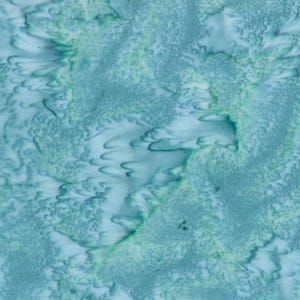 May include: Abstract fabric with a watercolour effect. The design features a blend of light blue, teal, and white, creating a textured, flowing pattern. The fabric's surface has a mottled appearance with organic shapes and subtle colour variations.