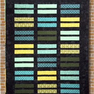 May include: A modern quilt with a black background and colorful rectangular blocks. The blocks are in shades of yellow, teal, and green, with various patterns. The quilt is labeled "Parallel Universe" and is displayed against a brick wall.