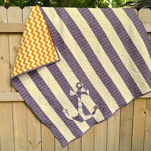 May include: A blue and white striped quilt with a large anchor design in the center. The back of the quilt is orange and white chevron.