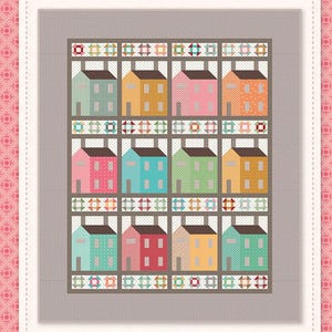 May include: A colorful quilt featuring a village scene with rows of houses in various colors, including pink, blue, and yellow. The quilt has a gray border and is labeled "Prim Village Quilt" by Riley Blake Designs.