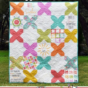 May include: A white quilt with a cross-stitch design featuring colorful X shapes and inspirational text. The quilt includes the phrases "Hello Sunshine" and "There is Sun in my Soul Today". The quilt is made by Running Doe Quilts.