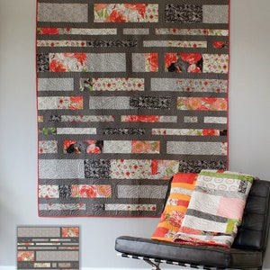 May include: A quilt pattern called "Sliding Shoji Screens" by Color and Quilt by Robin Pickens. The quilt features a geometric design with gray, white, and red fabric. The quilt is hanging on a wall above a black leather chair.