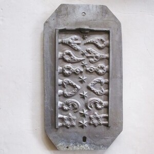 May include: A rectangular, gray metal mold with a series of decorative key designs and star accents. The mold features various key shapes, including ornate, heart-shaped, and floral designs. The metal has a weathered appearance.