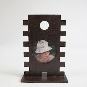 May include: A brown metal picture frame with a cutout design. The frame holds a photo of a person wearing a white hat.