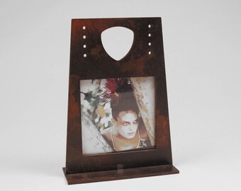 May include: A rustic brown metal picture frame with a cutout heart shape at the top. The frame holds a photo of a woman with a flower in her hair.