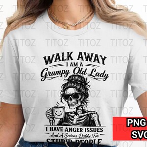 Puede incluir: Camiseta blanca con el texto "WALK AWAY I AM A Grumpy Old Lady". El gráfico presenta un esqueleto con gafas de sol sosteniendo una taza de café con una carita sonriente. La camiseta también tiene el texto "I HAVE ANGER ISSUES And A Serious Dislike For STUPID PEOPLE."