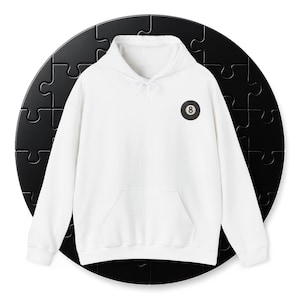 Puede incluir: Una sudadera con capucha blanca con un bolsillo delantero y una capucha con cordón. La sudadera tiene un parche en blanco y negro con el número 8, que se asemeja a una bola de billar. La prenda está hecha de un material suave.