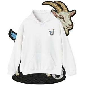 Könnte beinhalten: Ein weißer Kapuzenpullover mit Kängurutasche und einem kleinen, gestickten Ziegenlogo auf der Brust. Das Bild enthält auch einen Ziegenkopf-Aufnäher und einen Fußball-Themen-Aufnäher.