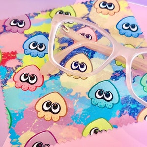 May include: A pink microfiber cleaning cloth with a colourful pattern of cartoon squids. A pair of pink-framed spectacles are lying on top of the cloth.