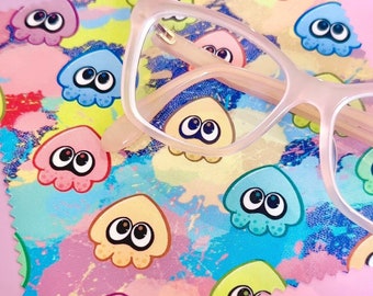 May include: A pink microfiber cleaning cloth with a colorful pattern of cartoon squids. A pair of pink-framed eyeglasses are lying on top of the cloth.