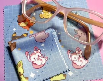 May include: A blue microfiber cleaning cloth with a grid pattern and cartoon characters printed on it. The cloth is folded in half and a pair of pink glasses with gold accents is lying on top of it.