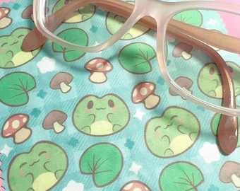 May include: A blue and green microfiber cleaning cloth with a repeating pattern of frogs, mushrooms, and lily pads. The cloth is designed to clean eyeglasses.