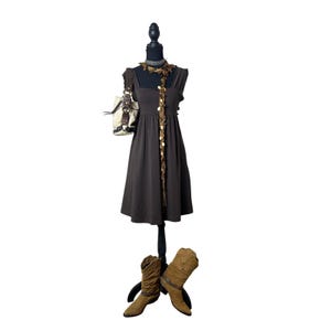 May include: A brown dress with a square neckline and a flowing skirt is displayed on a black mannequin. A cream-colored purse hangs on the mannequin's arm. Brown cowboy boots are at the base of the mannequin.