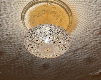 May include: A gold-toned, round, decorative ceiling light fixture with a patterned design. The light fixture is hanging from the ceiling and casting a shadow on the ceiling.
