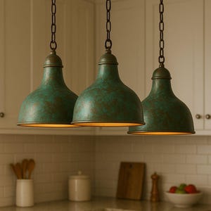 May include: Three teal-coloured pendant lights with bell-shaped shades hang from chains. The shades have a textured, mottled appearance. The lights are suspended above a kitchen countertop, suggesting a kitchen lighting fixture.