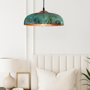 May include: A ceiling pendant light with a domed shade. The shade has a textured, weathered finish in green and copper tones. The light hangs from a black cord. The word "Achgalo" is printed at the bottom of the image.