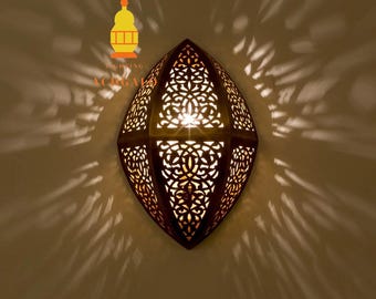 May include: A decorative wall sconce with a dark bronze finish and intricate cut-out patterns. The sconce emits a warm light, casting decorative shadows on the wall. The design features a Moroccan-inspired aesthetic, perfect for adding ambiance to any room.