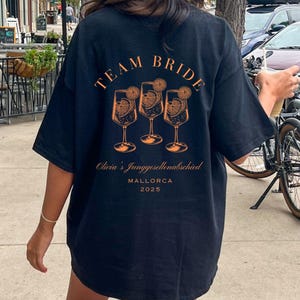 JGA T-Shirt The Bride & Team Bride – personalisiert mit Name Ort Jahr – Junggesellinnenabschied Braut Crew Party Shirt Schwarz "TEAM BRIDE"