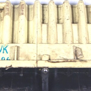 Op de afbeelding: Gebroken witte elektronische component met een geribbelde bovenkant en een zwarte basis. De component heeft de tekst "WK 0806" in blauw. Een zwarte connector is zichtbaar aan de linkerkant. Het item lijkt gebruikt.