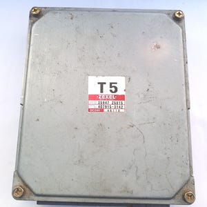 May include: A rectangular, silver-colored electronic control unit (ECU) with a label that reads "T5" and "Zexel". The label also includes numbers and "DC24V". The ECU is secured with four gold-colored screws.