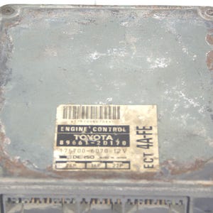 May include: A rectangular, grey Toyota engine control module. The label reads "ENGINE CONTROL TOYOTA 89661-2D170". The module shows signs of wear, with rust and discolouration visible on the surface.
