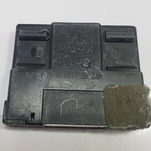 May include: A rectangular black plastic component with text and a foam pad attached. The component has various molded features, including a series of rectangular and circular openings. The text includes "CAV1" and "VP76EF 14B128 A".