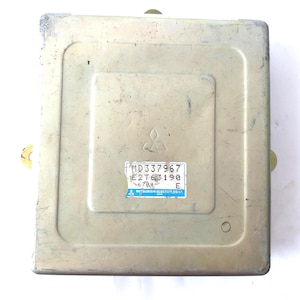 May include: A rectangular, metallic-coloured automotive computer module. The module has a recessed central panel with a Mitsubishi logo and a label with text including "MD337967" and "E2T63190".