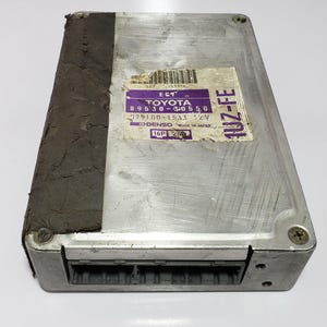 May include: A silver Toyota 1UZ-FE engine control unit (ECU) with a black label that reads "ECT TOYOTA 89530-30550 279100-1533 12V DENSO MADE IN JAPAN 16P 261".