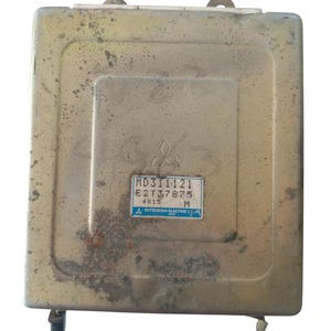 May include: A rectangular, metallic-toned automotive component with a slightly worn look. It features a central recessed section with a Mitsubishi logo and a label showing "MD311121" and other codes. This is likely an electronic control unit.