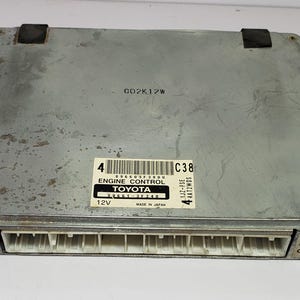 以下が含まれることがあります： 「CO2K12W」、「ENGINE CONTROL」、「TOYOTA」、「32561-37240」、「12V」、「MADE IN JAPAN」、「C38」、「1JZ-FSE」、「44AT2WOS」と印刷された銀色のエンジンコントロールユニットです。