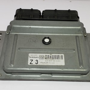 Op de afbeelding: Een zilverkleurige Nissan Z3 motorregeleenheid (ECU) met zwarte connectoren. De ECU heeft een rechthoekige vorm met montagegaten en een label met tekst en een barcode. De unit is ontworpen voor automobieltoepassingen.