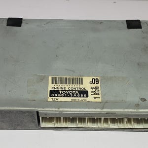 以下が含まれることがあります： 89651-3A680 と「ENGINE CONTROL」の文字が印刷された灰色のトヨタエンジンコントロールユニット。ユニットの下部に黒いコネクタがあり、右側に「11JZ-6 447000 C09」の文字が書かれたラベルがあります。