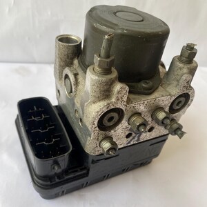 Op de afbeelding: Een gebruikte ABS-module, met een donkergroene cilindrische bovenkant en een zilverkleurige behuizing. Het heeft meerdere poorten en connectoren, met een zwarte rechthoekige connector aan de linkerkant. Het ontwerp is industrieel en mechanisch.