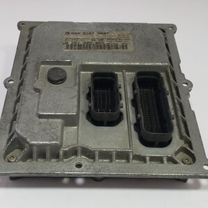 Può includere: Una centralina elettronica (ECU) color argento con due connettori neri e un'etichetta. La centralina ha una forma rettangolare con angoli arrotondati e diversi fori per viti. L'etichetta include testo e un codice a barre.