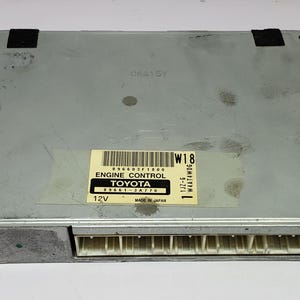 May include: A gray automotive engine control unit with a black label that reads "ENGINE CONTROL TOYOTA 89661-3A770 MADE IN JAPAN 12V W18 1JZ-GE WATANABE".