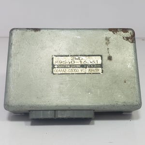 Könnte beinhalten: Ein rechteckiges, hellgraues elektronisches Steuergerät mit einem Etikett mit der Aufschrift "2WD 89540-16361 SUMITOMO ELECTRIC MADE IN JAPAN". Das Gerät hat einen Stecker und etwas Rost.