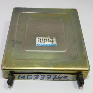May include: A gold-coloured metal box with a label that reads "MD33749 E2T37880 6604 MITSUBISHI ELECTRIC CORP.". The box has a black sticker on the bottom with the text "MD33749".