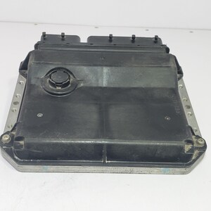 以下が含まれることがあります： 長方形の黒い電子制御ユニット（ECU）。ECUは中央に円形のコンポーネントがあり、上部にいくつかのコネクタがあります。ネジ穴のある銀色の金属フレームに取り付けられています。