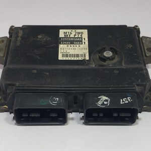 May include: A black electronic control unit (ECU) with multiple connectors and a label with text. The ECU has a rectangular shape with metal mounting brackets on the sides. The label includes model and part numbers.