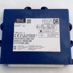 Könnte beinhalten: Ein blaues Toyota Smart Key-Modul mit weißen Etiketten und schwarzem Text. Das Modul trägt den Text "SMART KEY TOYOTA" und andere technische Informationen. Das Modul ist mit "TMLF8-2" und "ABS" beschriftet.
