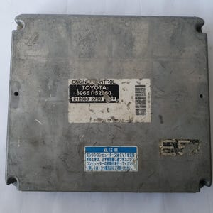 May include: A silver Toyota engine control module. The rectangular module has rounded corners and mounting points. The label reads "ENGINE CONTROL TOYOTA 89661-52060 212000-2750 2V". Japanese text is also visible on the module.