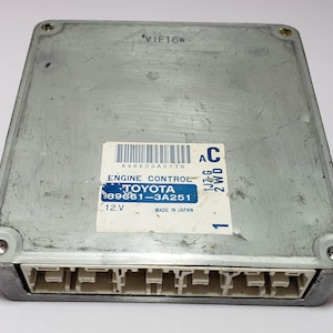 May include: A silver engine control unit with a black label that reads "896603A5710 ENGINE CONTROL TOYOTA 89661-3A251 12V MADE IN JAPAN" and a blue label that reads "AC 1JZ-G 2WD 1 VIF16W".
