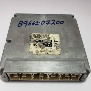 May include: A silver automotive engine control unit with the part number 89661-07200 printed on the top. The unit has a rectangular shape with a series of connectors on the bottom.