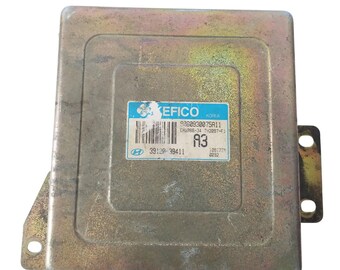 May include: A rectangular, metallic-colored car engine control unit (ECU) with a blue and white label. The label includes the text "KEFICO KOREA", a barcode, and other alphanumeric codes. The ECU has mounting brackets.