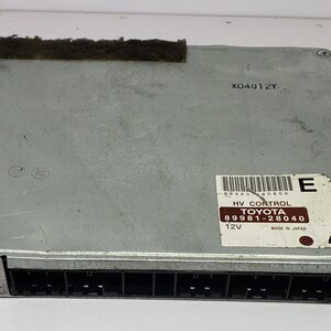 May include: A silver-colored Toyota HV Control module with a black connector. The module has a label with the Toyota logo, part number 89981-28040, and 12V specifications. The text "MADE IN JAPAN" is also visible.