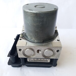 Op de afbeelding: Een zilver-zwarte automotive ABS (Anti-lock Braking System) module. De module heeft een cilindrisch component aan de bovenkant en een rechthoekige basis met diverse poorten en connectoren. Ontworpen voor automotive toepassingen.
