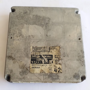 May include: A silver engine control unit, rectangular with rounded corners. A label shows "ENGINE CONTROL" and "TOYOTA". The unit has a worn appearance. Measurements are not available.