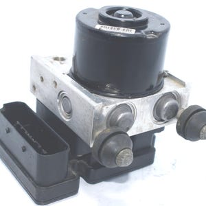 Op de afbeelding: Een antiblokkeersysteem (ABS)-module, met een zwart cilindrisch onderdeel bovenop een zilverkleurige metalen behuizing. De module heeft meerdere poorten en een zwarte rechthoekige connector. Ontworpen voor automobieltoepassingen.