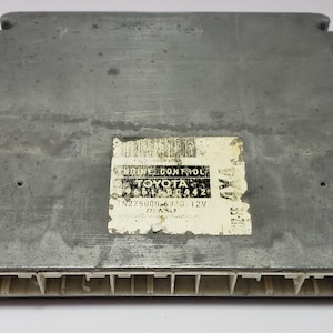 Può includere: Un'unità di controllo motore argentata con un'etichetta bianca che recita "ENGINE CONTROL TOYOTA 89661-0C462 12V DENSO".