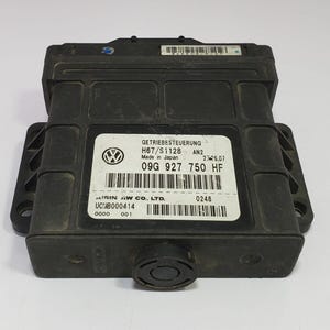 Könnte beinhalten: Ein schwarzes elektronisches Steuergerät mit rechteckiger Form. Das Modul hat mehrere Etiketten mit Text und Barcodes. Das Volkswagen-Logo ist auf einem der Etiketten zu sehen. Das Modul ist wahrscheinlich ein Autoteil.